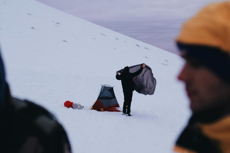 A person sets up a tent in a snowy mountain area during winter, illustrating outdoor adventure.