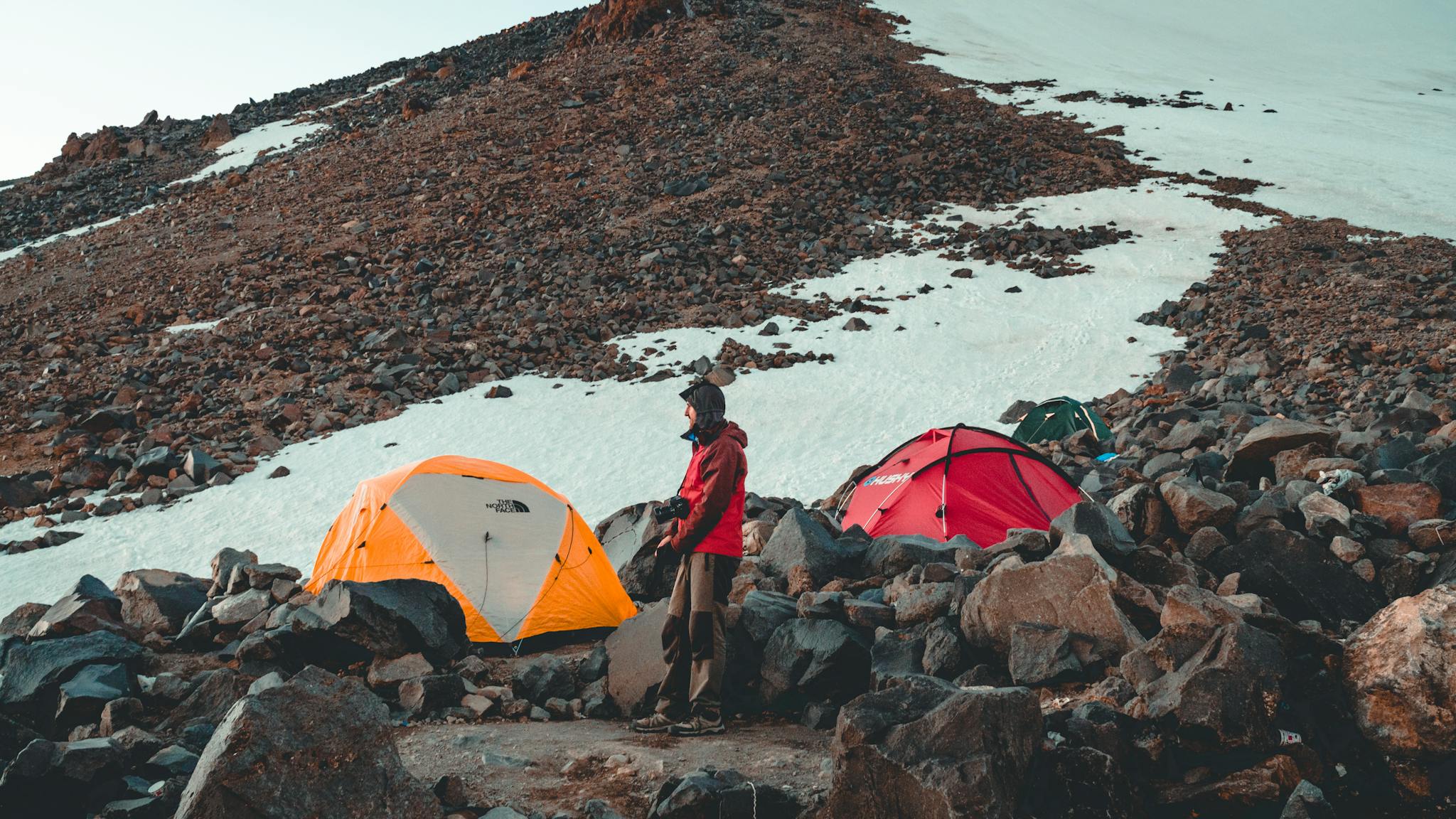 A person stands by colorful tents in a snowy mountain terrain, capturing the spirit of adventure.