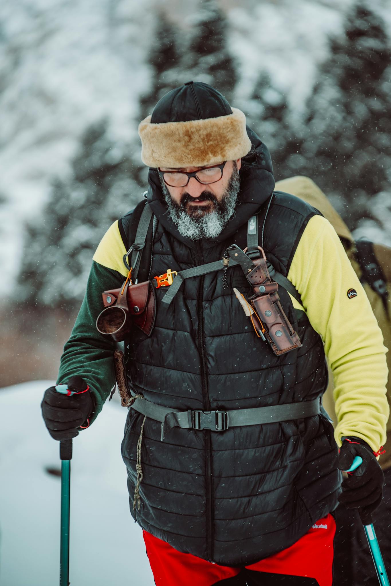 Bearded man hiking in winter wilderness with gear and snow background.