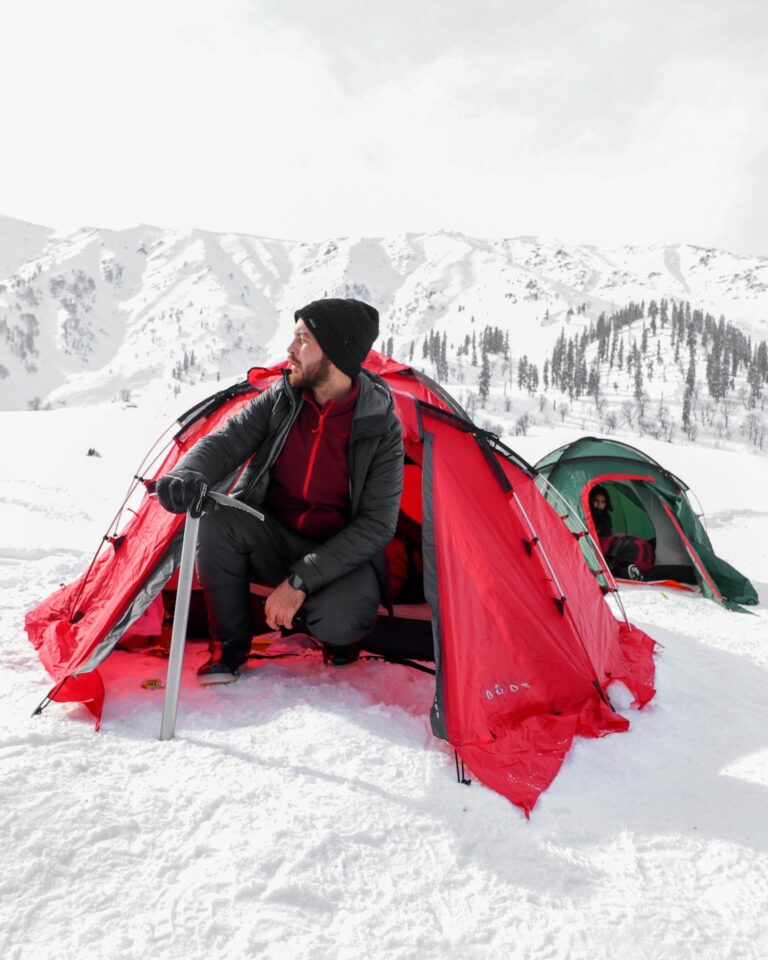 Man camping in snowy mountains with red tent. Explore winter adventure.