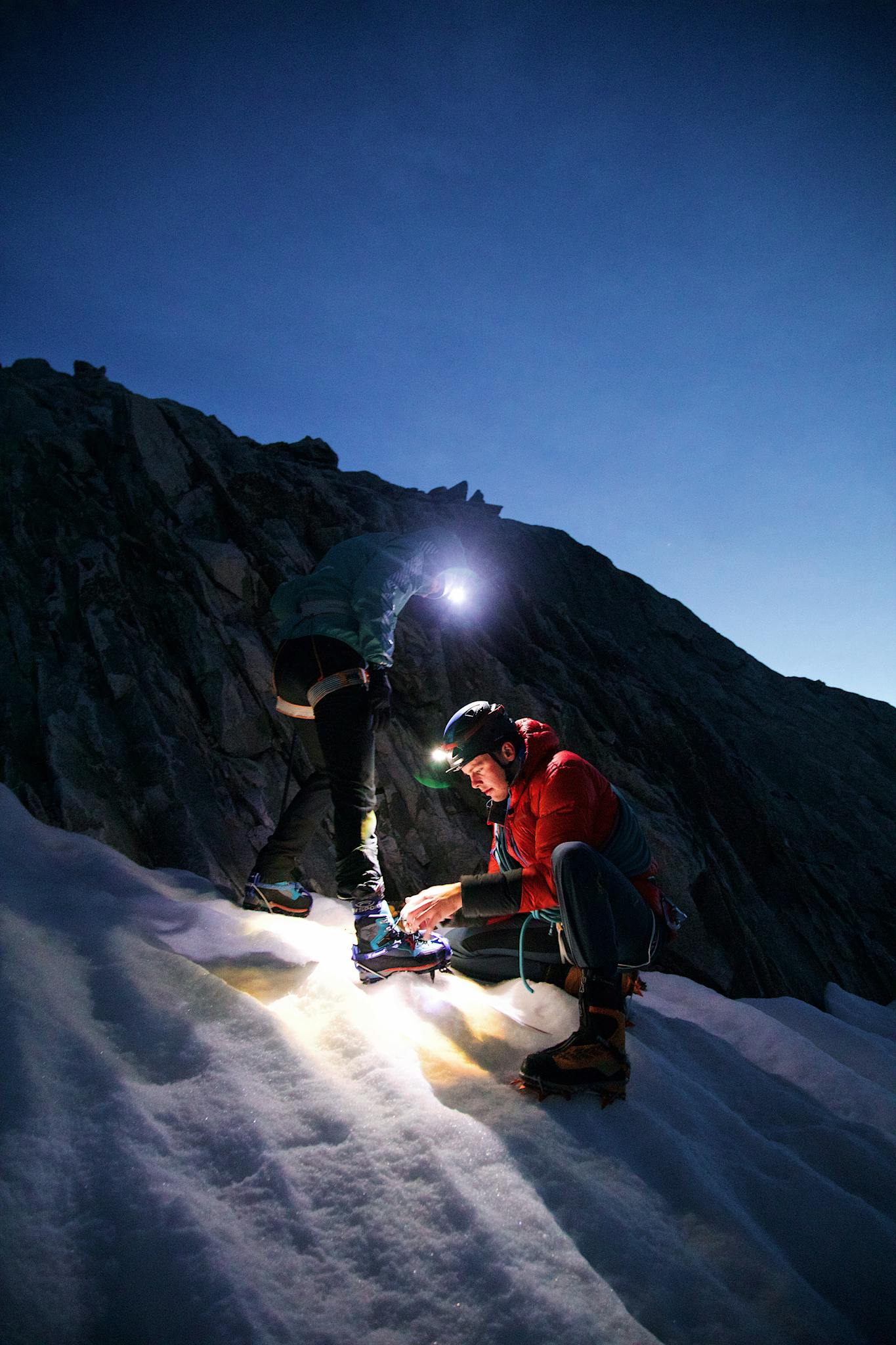 Two climbers explore a snowy mountain at dusk, lighting their path.