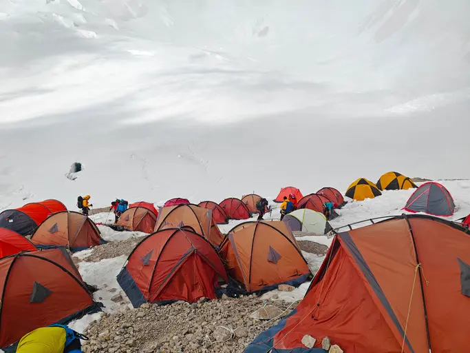 Mountaineering tents pitched on a snowy slope at Everest Base Camp with climbers in the background.