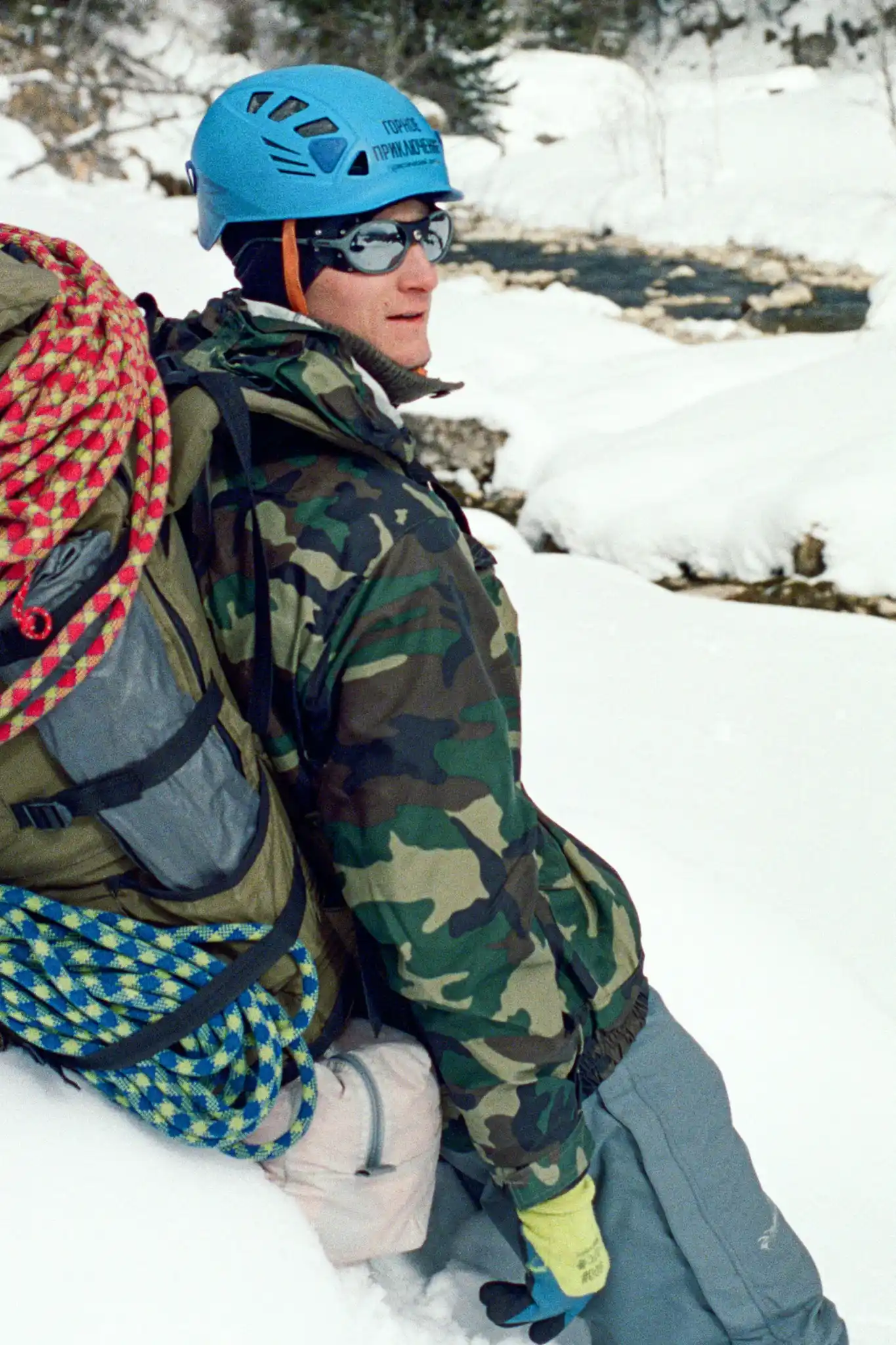 Male climber resting with full climbing gear and rope in snow.