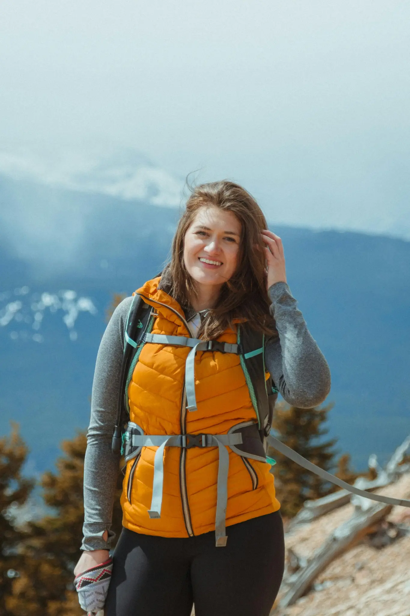 Female trekker smiling in an orange jacket on a scenic mountain trail.